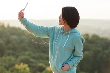 Güzel genç Japon kadın selfie açık telefonunu kullanarak ve gülümseyen parkta alarak