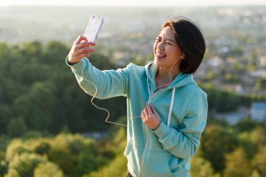 Şehvetli genç Japon kadın selfie açık telefonunu kullanarak ve gülerek parkta alarak