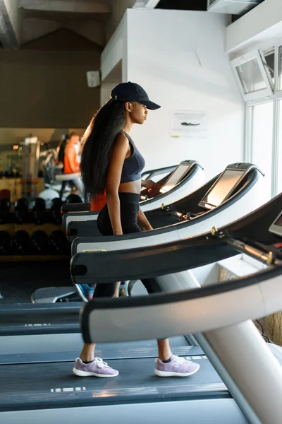 Courir sur un tapis roulant dans une salle de gym ou un club de fitness - femme noire sexy faisant de l'exercice pour gagner en forme — Photo