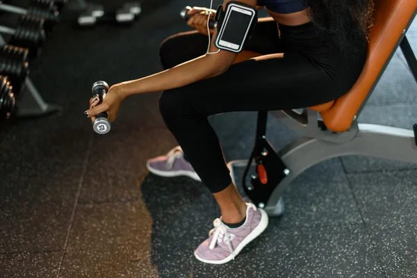 Gros plan mains de femme afro-américaine fitness sexy travaillant avec des haltères à la salle de gym et écoute de la musique dans les écouteurs — Photo