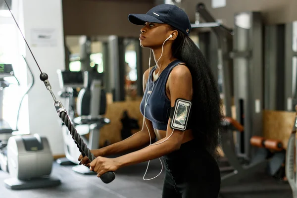 Vista lateral de la hermosa mujer afroamericana sexy haciendo ejercicio en el gimnasio y escucha música en auriculares blancos — Foto de Stock