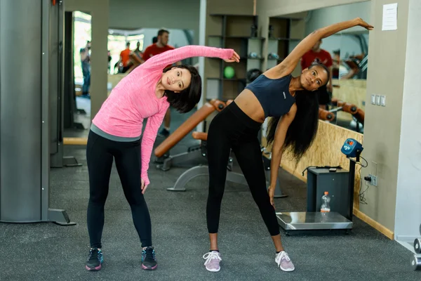 Vista lateral de delgado negro afroamericano fitness instructor y asiático encantadora mujer haciendo ejercicio trabajar juntos en el gimnasio —  Fotos de Stock