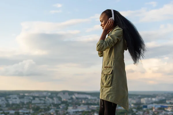 Schitterend lachende Afrikaans Amerikaans meisje luistert muziek en ontspannen. Stadsgezicht achtergrond wazig. Outdoor Portret — Stockfoto