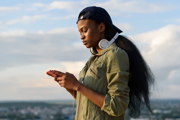 Güzel afro-amerikan kız müzik dinlemek ve sahiptir. Bulanık şehir arka plan üzerinde Gülümseyen genç siyah kadın
