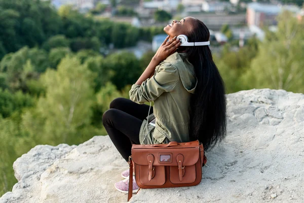 Momento di vera pace e armonia. Una giovane donna afroamericana che ascolta musica su uno sfondo blu cielo nuvoloso. Paesaggio roccioso — Foto Stock