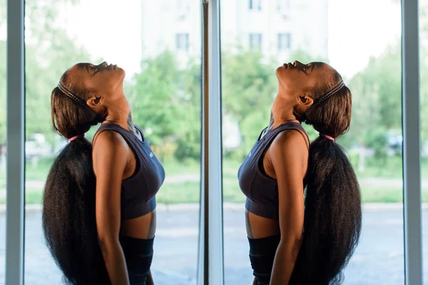 Vista lateral da bela jovem negra afro-americana com longos cabelos escuros olhando para o espelho no ginásio e relaxante — Fotografia de Stock