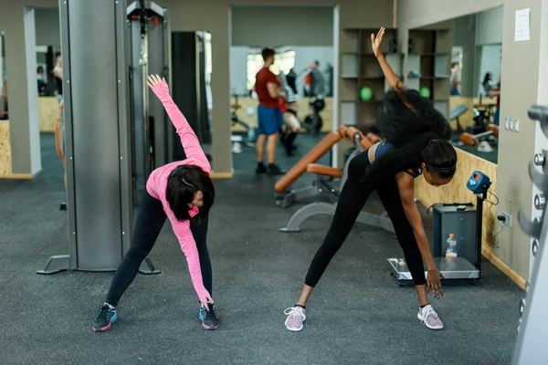 Тонкий черный африканско-американский инструктор по фитнесу показывает азиатской прекрасной женщине, как делать упражнения. Спортивный зал — стоковое фото