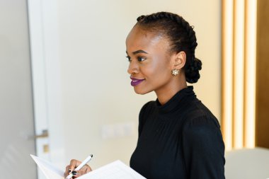 Işık ofiste beyaz not defteri ve kalem tutan parlak mor dudaklar ile gülümseyen güzel iş kadını Yan görünümü