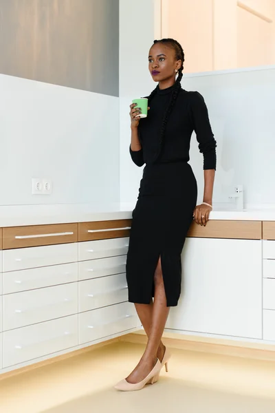 Полнометражный портрет деловой женщины в черном платье и бежевых туфлях с одноразовой чашкой во время работы в светлом офисе — стоковое фото