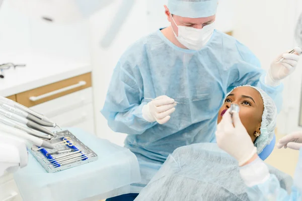 Стоматолог с ассистентом в форме делает медицинские процедуры пациентка в стакане для мусора в стоматологической клинике — стоковое фото