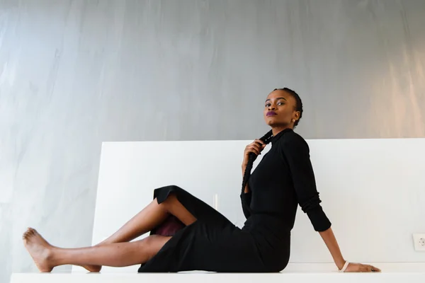 Elegante Afrikaanse of zwarte Amerikaanse vrouw in donkere kleding poseren op Bureau in lichte interieur — Stockfoto