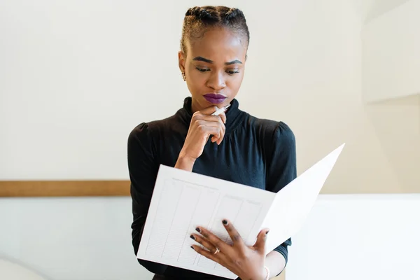 Close-up πορτρέτο της σκέψης επιτυχής Αφρικής ή μαύρο αμερικανικές επιχειρήσεις γυναίκα που κρατά ένα μεγάλο λευκό αρχείο και στυλό κοντά στο πηγούνι — Φωτογραφία Αρχείου