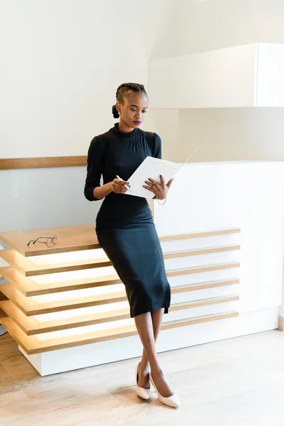 Stern κομψό Business γυναίκα φορώντας μαύρο φόρεμα και μπεζ παπούτσια στο ελαφρύ γραφείο κοιτάζοντας την ατζέντα της, πλήρους μήκους πορτρέτο — Φωτογραφία Αρχείου