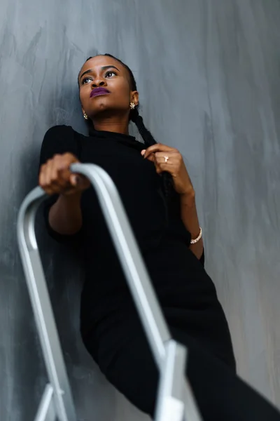 Young pretty black american woman touching her thick plait looking up on dark studio background