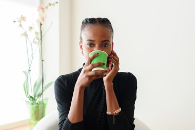 Kamera telefon ve tek kullanımlık Kupası pencere tutarak bakarak Elrgant Afrika veya siyah Amerikalı kadın