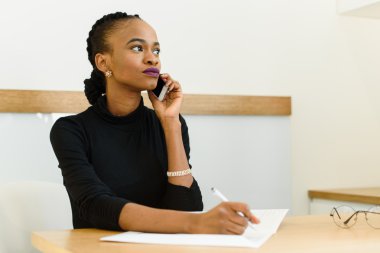 Ciddi kendine güvenen genç Afrika veya siyah üzerinde seyir telefon uzakta Office Not Defteri ile Amerikan iş kadını