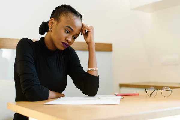 Nachdenkliche besorgte afrikanische oder schwarze Amerikanerin, die ihre Stirn mit der Hand auf den Notizblock im Büro hält — Stockfoto