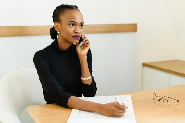 Sério confiante jovem Africano ou negro mulher de negócios americano no telefone olhando para longe com bloco de notas no escritório — Fotografia de Stock