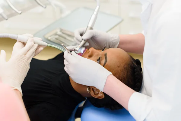 Вид сбоку стоматолога и медсестры, делающей профессиональную чистку зубов молодой пациентке в стоматологическом кабинете — стоковое фото