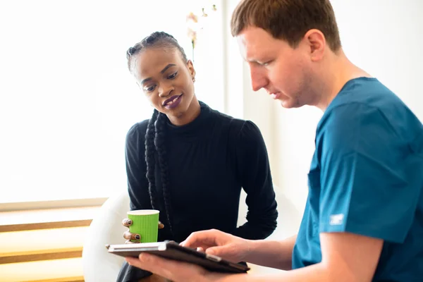 Young male dentist showing dental X-ray report on tablet to beautiful black female patient in clinic — Stock Photo, Image