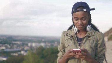 Yakın çekim portre güzel hipster Afro-Amerikan kız dinleme müzik açık. Bulanık cityscape arka plan