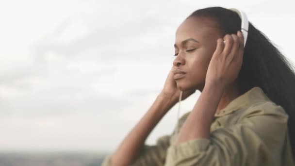 魅力的なアフリカ系アメリカ人の女性は音楽を聴くと、ぼやけた街背景でリラックス — ストック動画