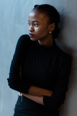 Gri arka plan üzerinde duran ve uzağa arıyorsunuz katlanmış silah ile ciddi bir Afrika veya siyah Amerikalı kadın portresi