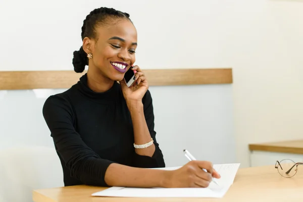 Lachende jonge zwarte zakenvrouw op telefoon aantekeningen in office — Stockfoto