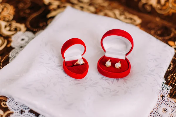 Conjunto de jóias mulheres elegantes: brincos e anel de dedo com pérolas em caixas vermelhas para cada um. Isolado em pano de seda branco. Toalha de mesa modelada em segundo plano — Fotografia de Stock