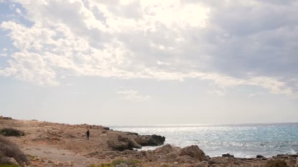 Man lopen door het rotsachtige strand op een mooie zonnige dag. Cyprus. — Stockvideo