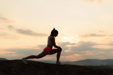 Sunset bulvarında açık germe uygun kaslı kadın silüeti. Fitness kavramı