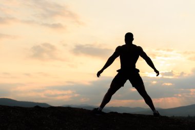 Gündoğumu veya günbatımı dağlarda poz vücut geliştirmeci silüeti. Güçlü yakışıklı kaslarına gösterilen