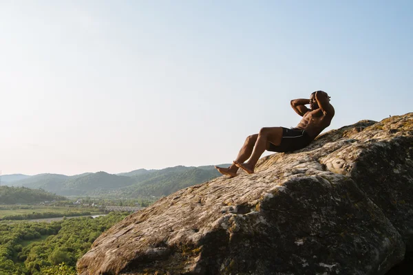 Gespierde sportieve zwarte man doen pers ups te vertrouwen op de rotsachtige piek. Adembenemende berg landschap achtergrond. Buiten trainingsconcept — Stockfoto