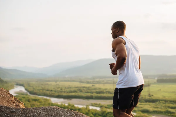 Zwarte Afrikaanse Amerikaanse gespierde mannelijk model bodybuilder joggen buiten. Groene Woud bergen op achtergrond — Stockfoto