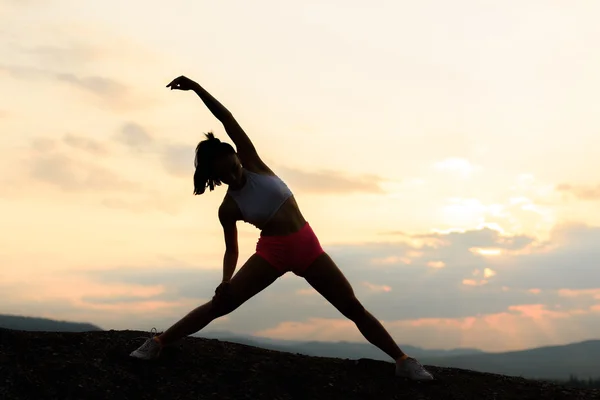 Silhouet van fitness vrouw uit te oefenen en rekken op mooie zomerse zonsondergang of 's morgens op strand. Vrouwelijke doen ontspannen yoga oefeningen — Stockfoto