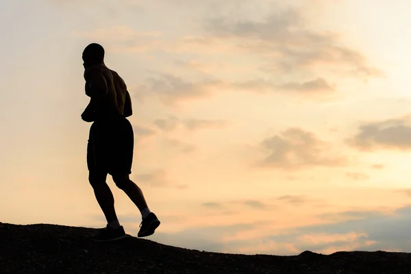 Siluett av amerikansk idrottsman jogging på solnedgången i bergen. Träning utomhus. Sport och fitness koncept — Stockfoto