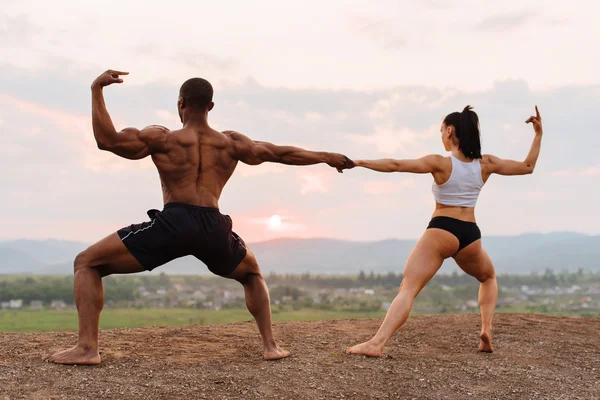 Gespierde Afro-Amerikaanse man en sexy brunette vrouw uitrekken samen op de berg landschap-achtergrond. — Stockfoto