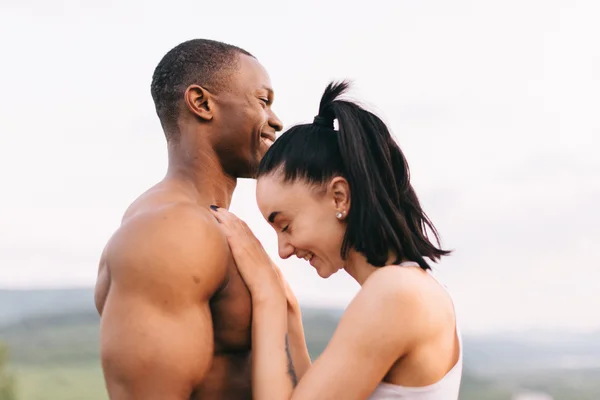 Close-up van sexy fit gemengd ras paar met perfecte lichamen in sportkleding zacht omarmen op bergen landschap-achtergrond. — Stockfoto