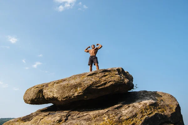 L'atleta afroamericano si erge su una roccia contro il cielo blu nuvoloso — Foto Stock