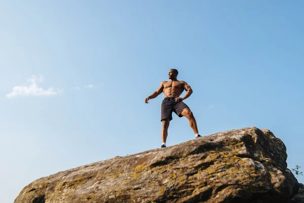 Topless portret van sterke zwarte Afrikaanse Amerikaanse man bodybuilder poseren op de rots. Blauwe bewolkte hemel achtergrond — Stockfoto