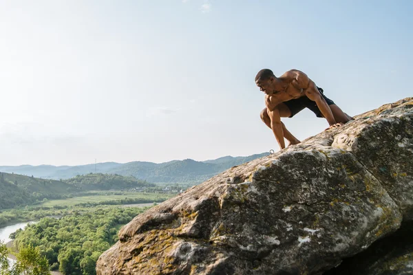 Ritratto emotivo di nero afroamericano bodybuilder uomo in posa sulla roccia con sfondo cielo blu. Stile natura selvaggia — Foto Stock