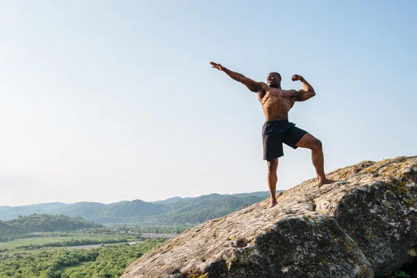 Zwarte Afro-Amerikaanse lachende atleet man op de rots in de bergen. Schoonheid en perfectie van het menselijk lichaam — Stockfoto