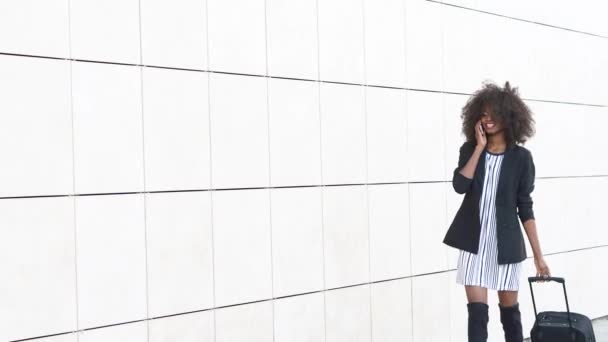 Elegante mujer afroamericana con equipaje en el aeropuerto. Fondo de pared con textura blanca. Preparándose para el viaje — Vídeos de Stock