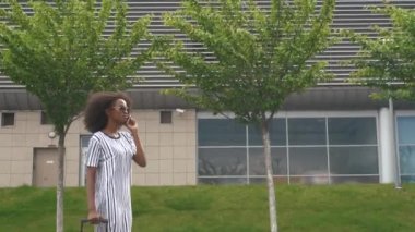 Havaalanında bir uçuş beklerken cep telefonu konuşurken güneş gözlüğü çekici genç gülümseyen Afrikalı Amerikalı iş kadını Yan görünümü.