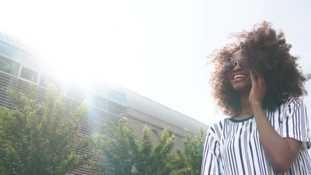 Bella giovane donna afroamericana con gli occhiali da sole che parla al telefono. Sfondo cielo — Video Stock