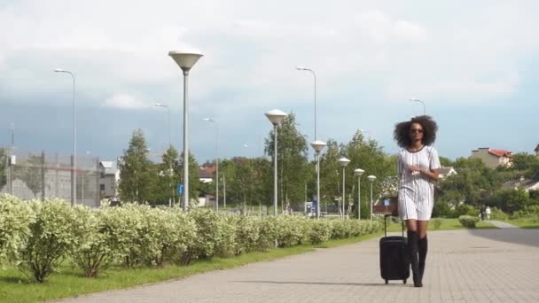 Ganzkörperansicht einer elegant lächelnden afrikanisch-amerikanischen Geschäftsfrau mit Sonnenbrille, die mit ihrem Gepäck zum Flughafen fährt. Geschäftsreisekonzept — Stockvideo