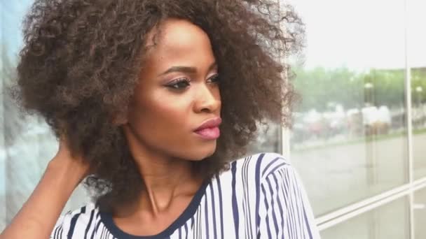 Портрет сексуальной чувственной молодой африканской модели с ярким макияжем, очаровательно улыбающейся на фоне стеклянной стены крупным планом — стоковое видео