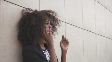 Çekici Afro-Amerikan iş kadınının telefonla konuşması ve beyaz dokulu duvara güvenerek yakın çekim