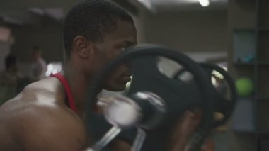 Barbell ile spor salonunda çalışan kas terli vücut geliştirmeci yan görünüm