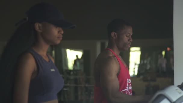 Gros plan vue de côté du couple noir afro-américain homme et femme courant ensemble sur des tapis roulants dans la salle de gym — Video